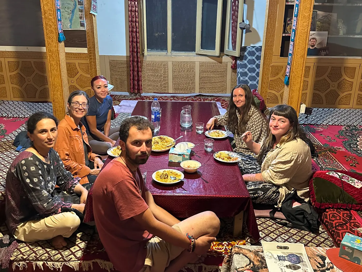 Guests sitting on the floor around the low table, eating together in the family's dining room
