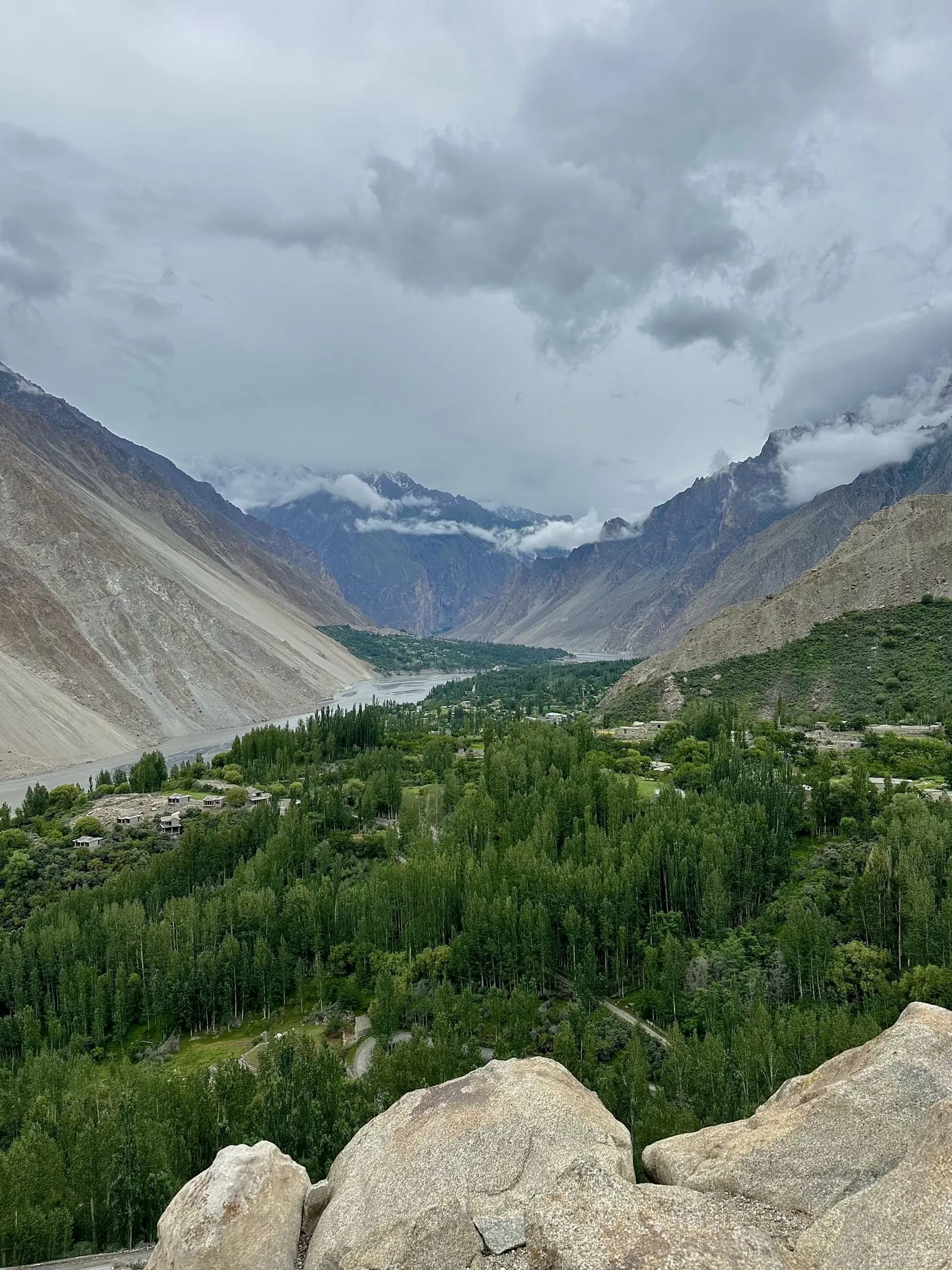 The Hunza valley under heavy cloud, green orchards and poplars along the river between bare mountain walls